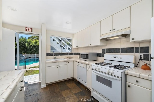 kitchen featuring white appliances, under cabinet range hood, decorative backsplash, and tile countertops