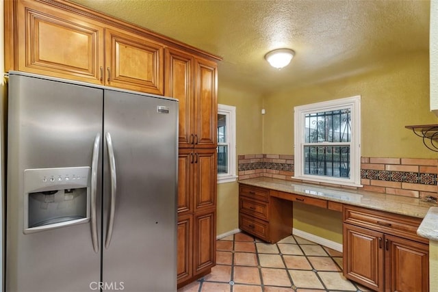 kitchen featuring tasteful backsplash, stainless steel refrigerator with ice dispenser, light stone countertops, and built in desk