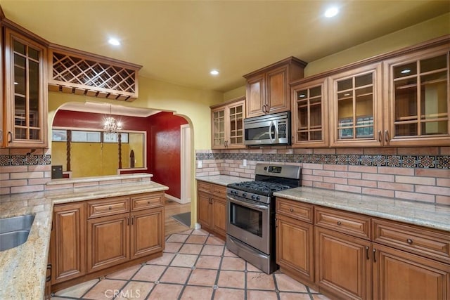 kitchen with tasteful backsplash, decorative light fixtures, light tile patterned floors, appliances with stainless steel finishes, and light stone countertops