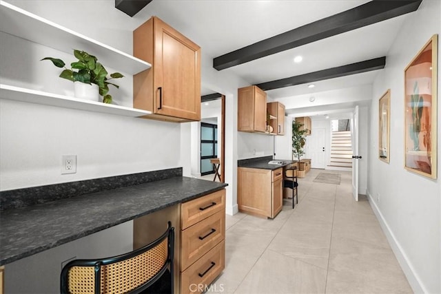 kitchen featuring dark stone countertops, a breakfast bar, built in desk, and beam ceiling