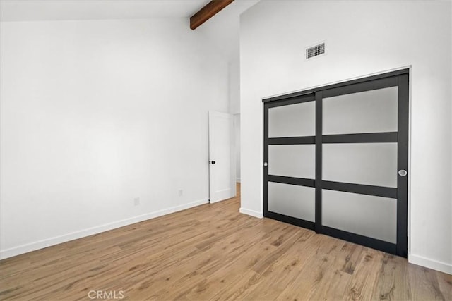 unfurnished bedroom with beamed ceiling, high vaulted ceiling, and light hardwood / wood-style floors