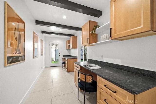 kitchen with beamed ceiling, dark stone countertops, built in desk, and light tile patterned floors