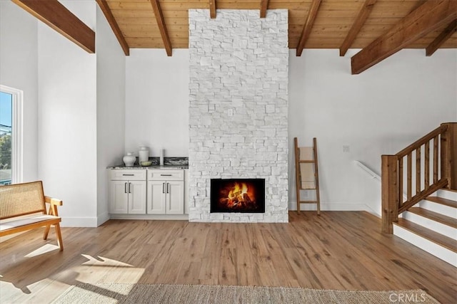 unfurnished living room featuring high vaulted ceiling, a fireplace, wooden ceiling, beam ceiling, and light hardwood / wood-style flooring