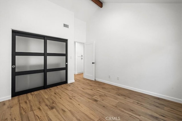 unfurnished bedroom with beamed ceiling, high vaulted ceiling, and light hardwood / wood-style floors