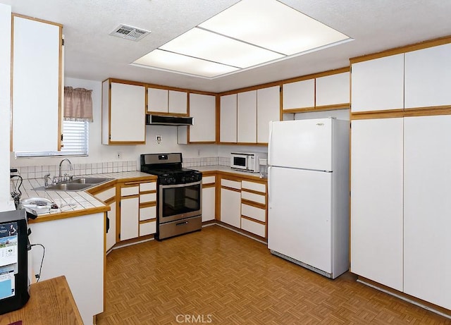 kitchen with sink, white appliances, light parquet floors, and white cabinets