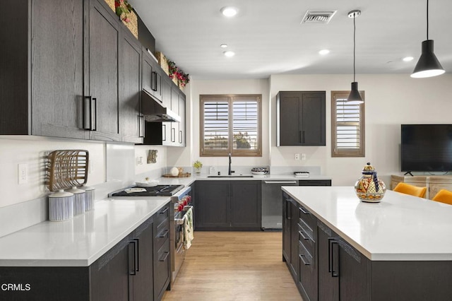 kitchen featuring sink, appliances with stainless steel finishes, hanging light fixtures, a center island, and light hardwood / wood-style floors