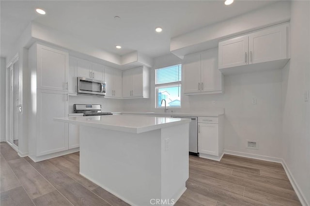 kitchen with stainless steel appliances, a center island, light wood-type flooring, and white cabinets