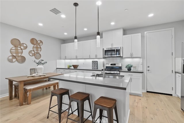 kitchen featuring white cabinetry, hanging light fixtures, an island with sink, and appliances with stainless steel finishes