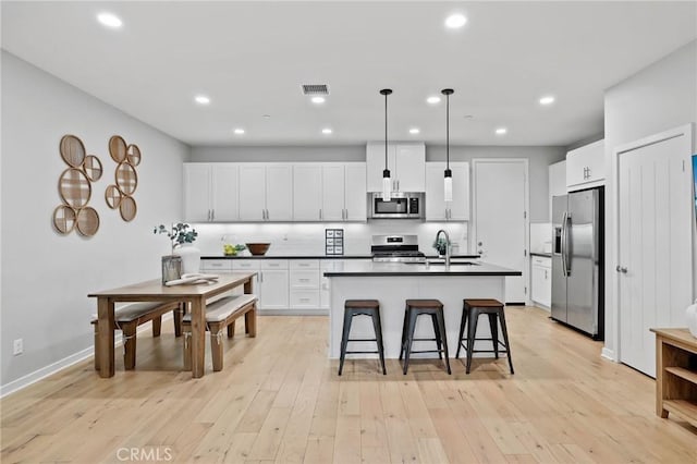 kitchen featuring sink, white cabinetry, hanging light fixtures, stainless steel appliances, and a center island with sink