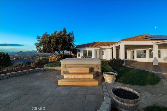 back of house with stucco siding, a hot tub, a ceiling fan, a patio area, and a tiled roof