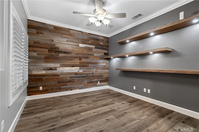 spare room featuring an accent wall, wood finished floors, visible vents, and crown molding