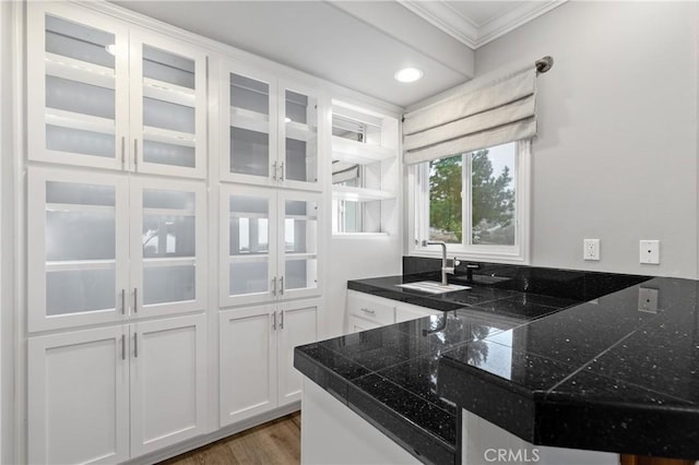 kitchen with light wood finished floors, glass insert cabinets, ornamental molding, white cabinetry, and a sink