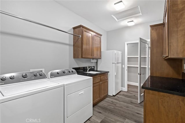 clothes washing area featuring cabinet space, attic access, wood finished floors, washer and dryer, and a sink