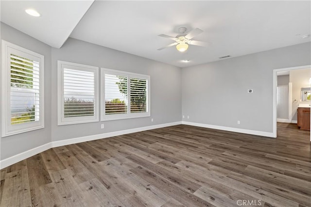 empty room featuring a ceiling fan, wood finished floors, visible vents, and baseboards