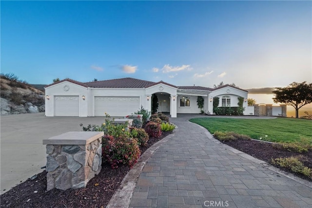 mediterranean / spanish-style house featuring a garage, driveway, a tiled roof, stucco siding, and a front lawn