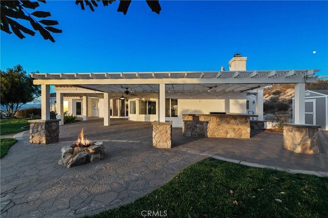 view of patio with outdoor dry bar, area for grilling, a ceiling fan, a pergola, and a fire pit