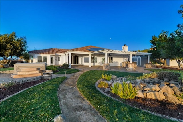 back of house featuring a patio, a chimney, stucco siding, solar panels, and a tiled roof