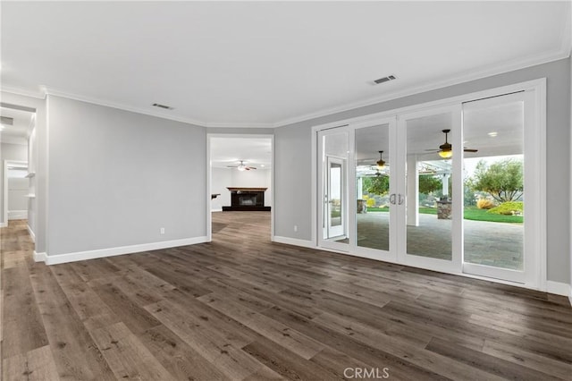 unfurnished living room with dark wood-type flooring, a glass covered fireplace, visible vents, and crown molding