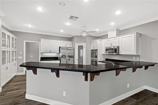 kitchen with a peninsula, appliances with stainless steel finishes, visible vents, and dark wood-type flooring