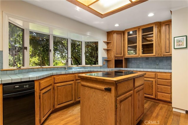 kitchen featuring tile counters, brown cabinetry, glass insert cabinets, a kitchen island, and black electric cooktop