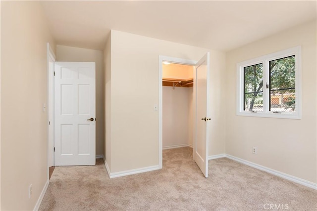 unfurnished bedroom with a spacious closet, baseboards, and light colored carpet