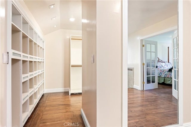 hall featuring lofted ceiling, baseboards, and wood finished floors