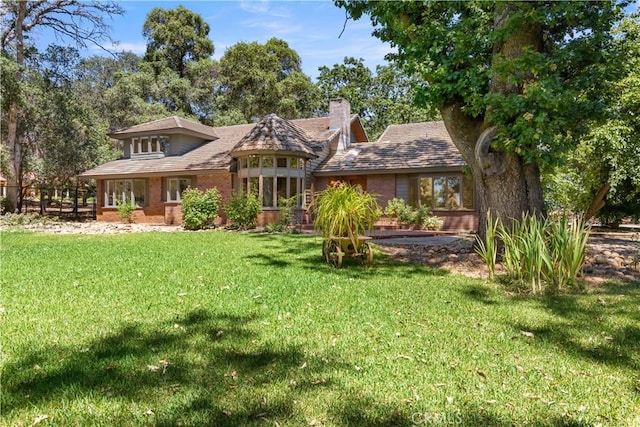 view of front of house featuring a front lawn, a chimney, and brick siding