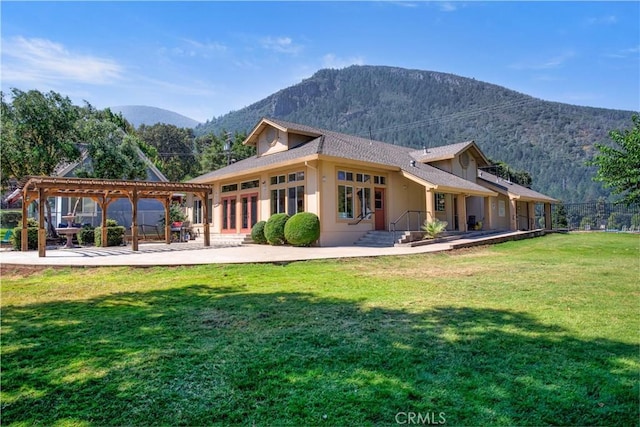 back of house featuring stucco siding, a mountain view, a patio, and a lawn