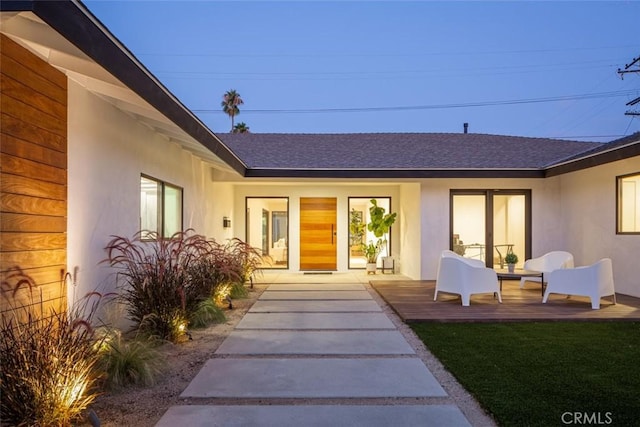 property entrance with a shingled roof and stucco siding