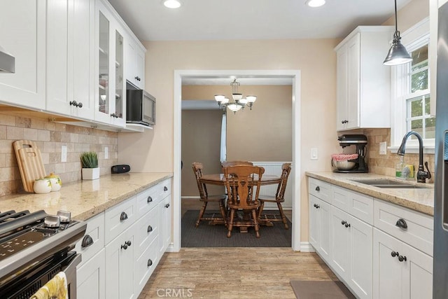 kitchen featuring white cabinetry, sink, hanging light fixtures, stainless steel gas range, and light wood-type flooring