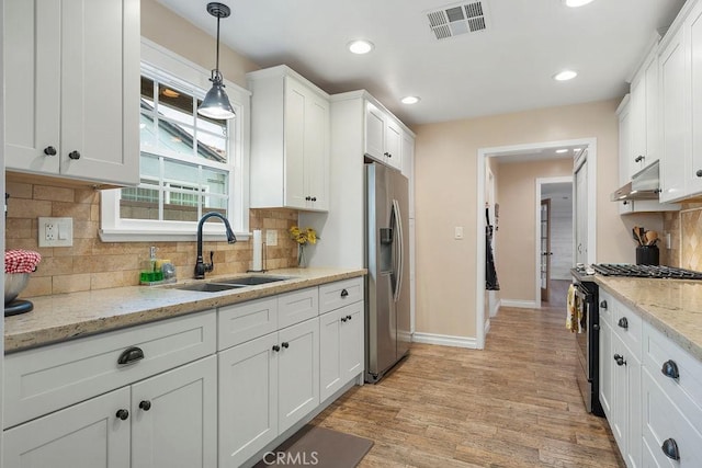 kitchen with black gas range oven, sink, hanging light fixtures, stainless steel refrigerator with ice dispenser, and white cabinets