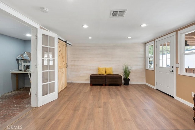 entryway with a barn door, wood walls, and light hardwood / wood-style flooring