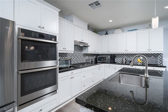 kitchen featuring sink, white cabinetry, dark stone counters, stainless steel appliances, and decorative backsplash