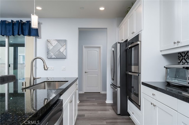 kitchen featuring sink, dark stone countertops, stainless steel appliances, white cabinets, and decorative light fixtures