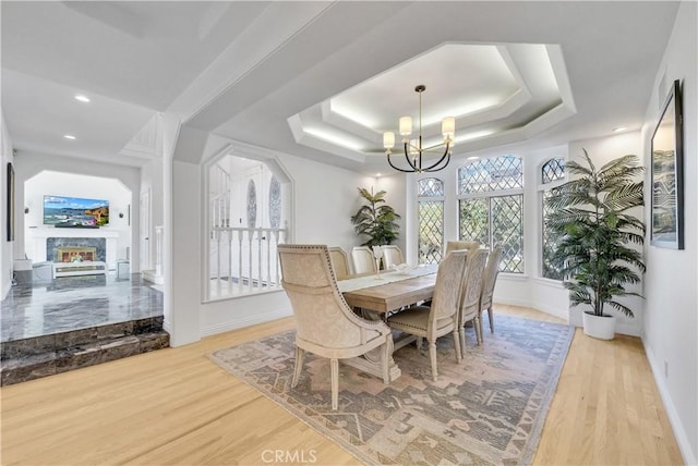 dining area featuring light wood finished floors, baseboards, a glass covered fireplace, an inviting chandelier, and a tray ceiling