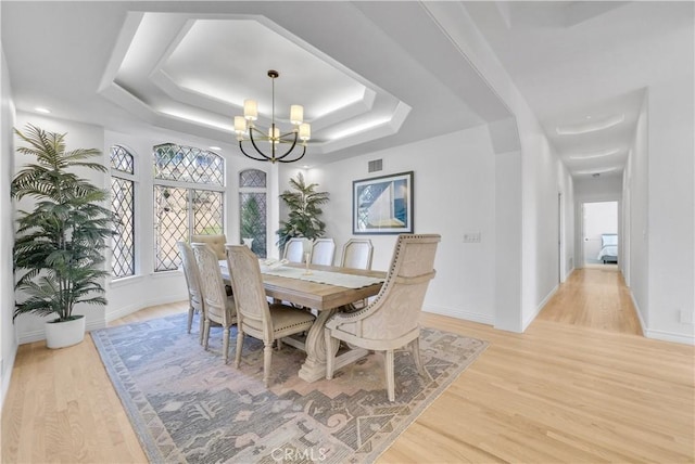 dining space featuring a chandelier, light wood finished floors, a raised ceiling, and visible vents