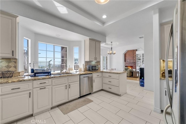 kitchen with stainless steel appliances, a sink, white cabinetry, and decorative light fixtures