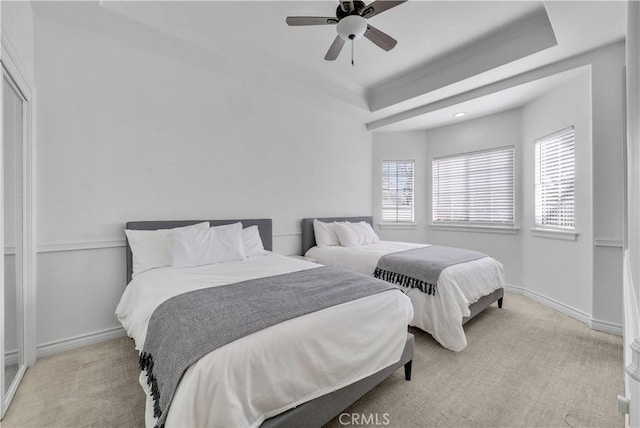 bedroom with ceiling fan, a tray ceiling, light colored carpet, and baseboards