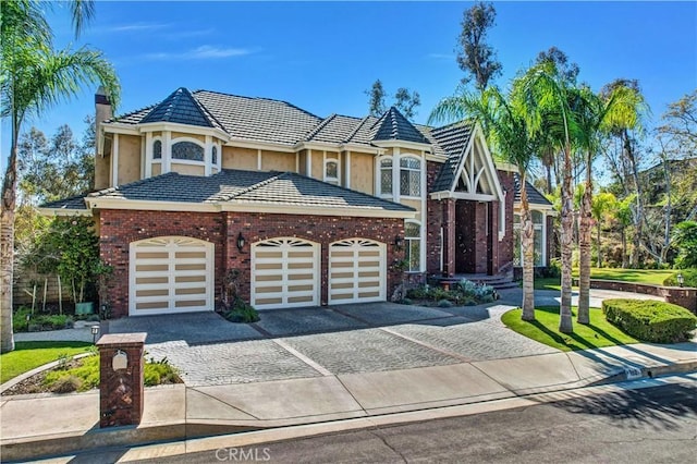 view of front of property with decorative driveway, a tile roof, brick siding, a chimney, and an attached garage