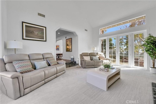 living room with light carpet, high vaulted ceiling, arched walkways, and visible vents