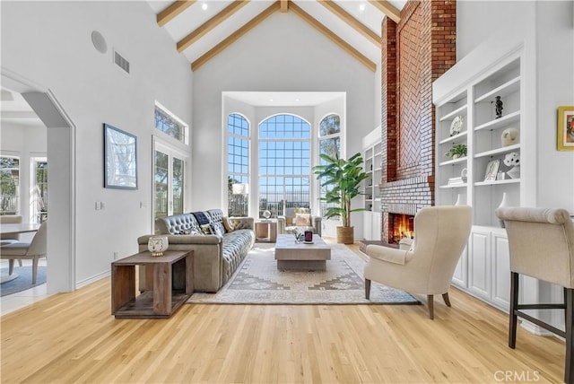 sitting room with a healthy amount of sunlight, a fireplace, beam ceiling, and light wood-style floors