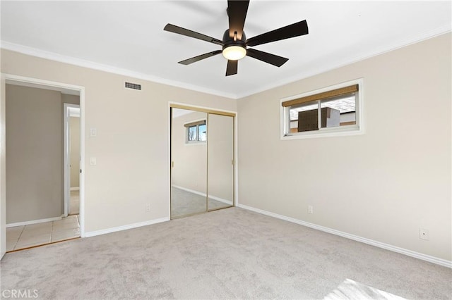 unfurnished bedroom featuring crown molding, light colored carpet, ceiling fan, and a closet