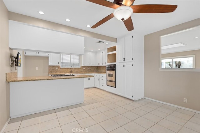 kitchen with oven, backsplash, white cabinets, light stone counters, and kitchen peninsula