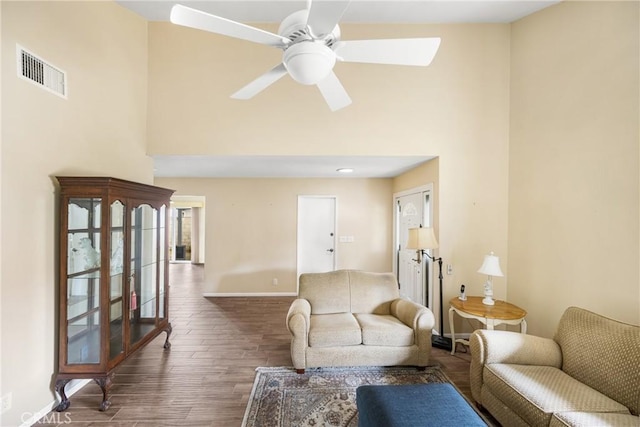 living room with dark hardwood / wood-style flooring, a towering ceiling, and ceiling fan