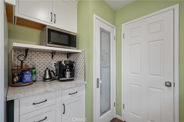 kitchen featuring tasteful backsplash, white cabinets, and light stone counters