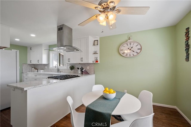 kitchen featuring island range hood, white cabinets, white refrigerator, light stone counters, and kitchen peninsula