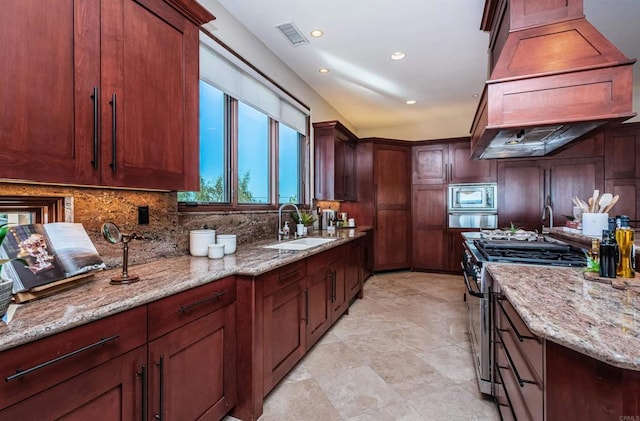 kitchen featuring sink, custom range hood, stainless steel appliances, light stone countertops, and decorative backsplash