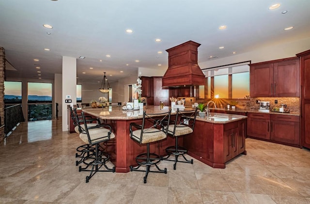 kitchen featuring sink, a breakfast bar area, backsplash, a large island with sink, and light stone countertops