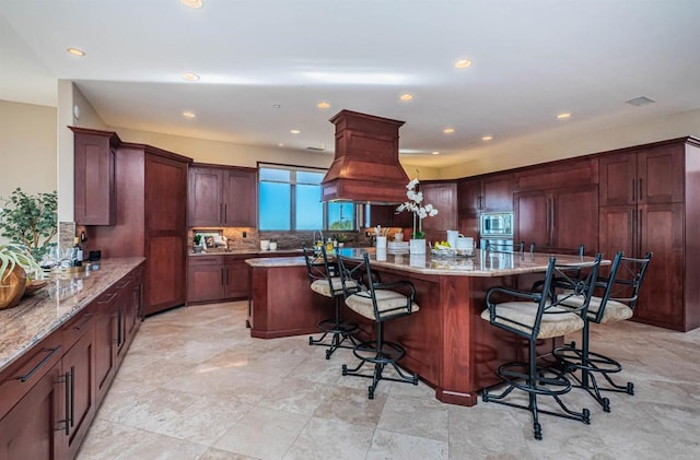 kitchen with a kitchen island, a breakfast bar, stainless steel microwave, backsplash, and light stone countertops