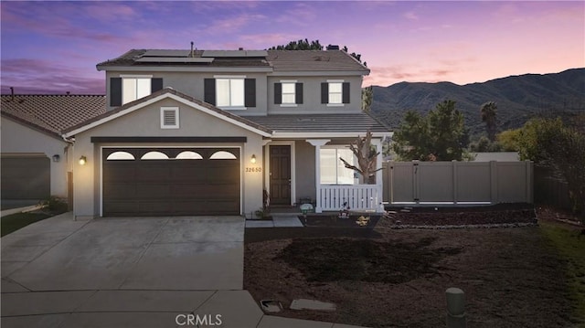 traditional-style home with concrete driveway, roof mounted solar panels, a mountain view, a porch, and stucco siding